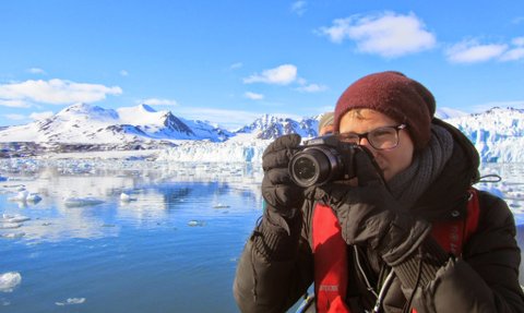 Eine Person mit einer Kamera steht am Wasser und fotografiert die beeindruckende Berglandschaft im Hintergrund.