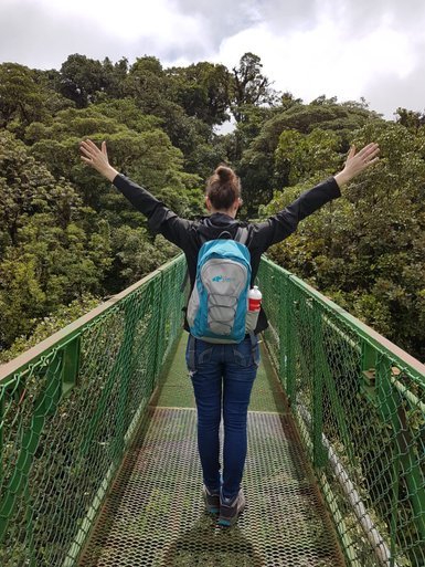 Eine Frau überquert eine Hängebrücke hoch über dem Boden im tropischen Regenwald – Costa Rica Reise mit Kindern