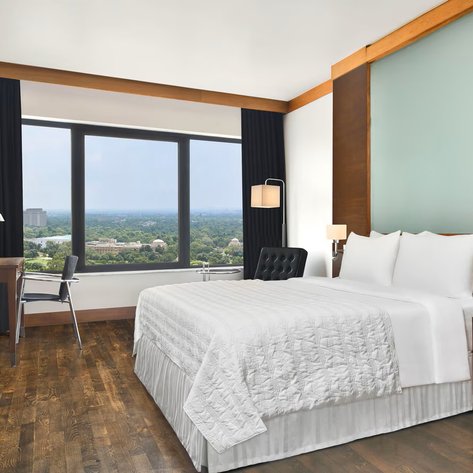 Ein modernes Hotelzimmer mit einem großen Fenster, das einen Blick auf die grüne Landschaft von Neu-Delhi bietet.