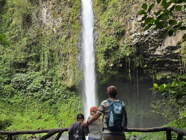 Eine Familie steht am Rand einer Aussichtsplattform und bestaunt einen majestätischen Wasserfall, umgeben von üppigem Grün.