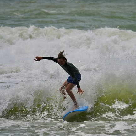 Ein junger Surfer mit kurz geschnittenen Haaren reitet geschickt auf einer grünen Welle und zeigt seine Begeisterung.