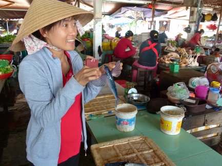 Einheimische präsentiert frischen Fisch auf einem belebten Markt – Vietnam mit Kindern