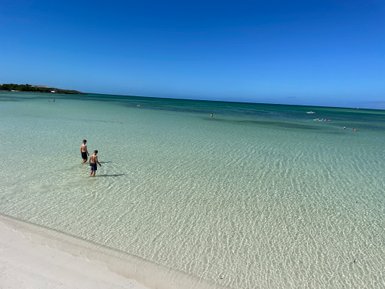 Zwei Jungen stehen im flachen Wasser eines klaren Strandes, umgeben von sanften Wellen und strahlend blauem Himmel.