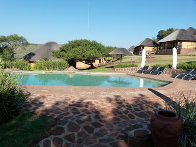 Ein einladender Pool in einem malerischen Lodge-Umfeld, umgeben von üppigem Grün und traditionellen Strohdächern.