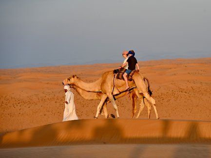 Beduin führt Kamele mit Mutter und Tochter durch die Wüste – Oman Familienreise