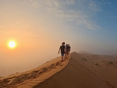 Familie wandert über eine hohe Sanddüne in der Wüste – Oman Familienreise
