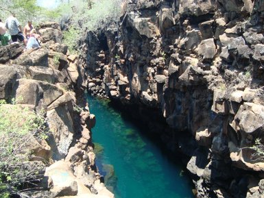 Eine schmale, türkisfarbene Wasserstraße zwischen hohen, rauen Felsen, umgeben von spärlicher Vegetation.