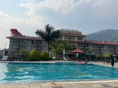 Ein Hotel mit einem großen Pool, umgeben von Palmen und grünen Sträuchern, bietet eine entspannte Urlaubsatmosphäre.