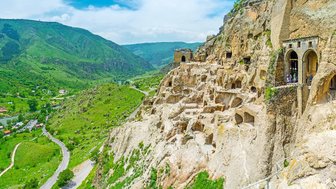Die beeindruckenden Höhlenwohnungen sind in die steilen Felsen einer grünen Landschaft eingebaut, umgeben von Bergen.