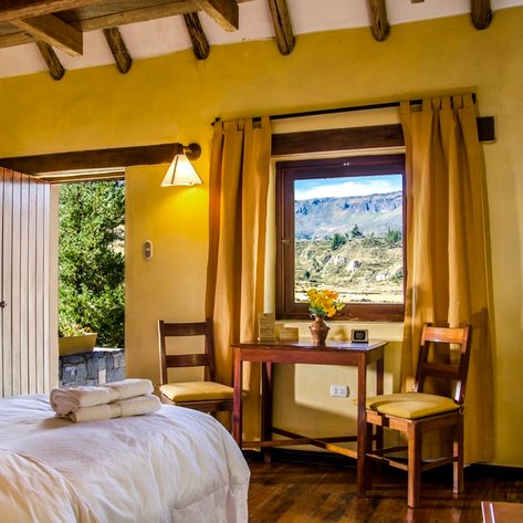 Ein gemütliches Zimmer mit zwei Betten, einem Tisch und Stühlen, das durch ein Fenster mit Blick auf die Berge erhellt wird.