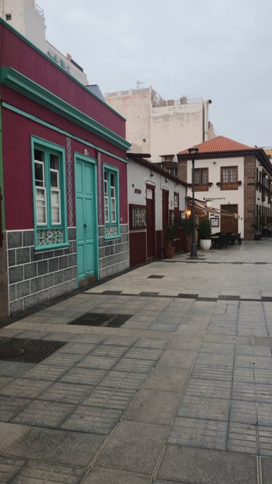 Bunte Gebäude mit einer türkisfarbenen Tür und einem gepflasterten Gehweg in einer ruhigen Straße in Puerto de la Cruz.