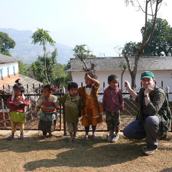 Eine Gruppe von Kindern steht fröhlich vor einem Zaun, während ein Erwachsener lächelnd neben ihnen posiert.