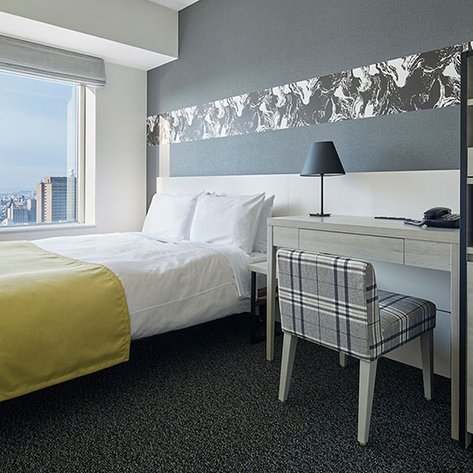 Ein modernes Hotelzimmer mit einem großen Fenster, das einen Blick auf die Stadt bietet, und einem gemütlichen Bett mit gelbem Überwurf.