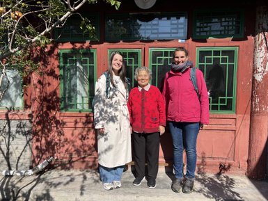 Drei Personen stehen vor einem traditionellen Hutong-Haus in Peking, umgeben von grünen Fenstern und einem sonnigen Tag.
