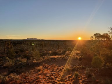 Ein spektakulärer Sonnenuntergang färbt den Himmel orange über der weiten Wüste und den sanften Hügeln im Hintergrund.