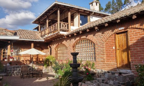 Eine charmante Hacienda mit roten Ziegelwänden, einem Innenhof und einem Brunnen, umgeben von Pflanzen und Blumen.