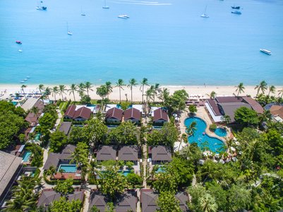 Eine Luftaufnahme eines Resorts mit mehreren Bungalows, umgeben von Palmen und einem klaren blauen Meer.