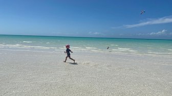 Mädchen läuft lachend durch das seichte Wasser am Strand – Mexiko mit Kindern