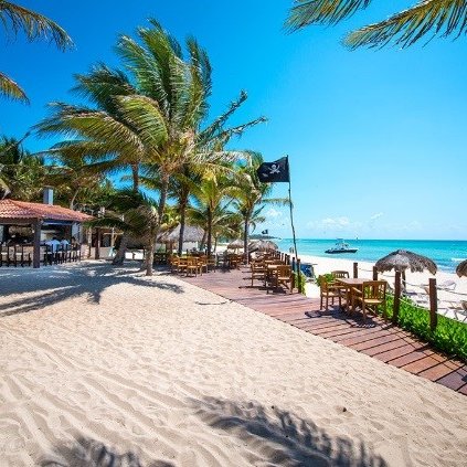 Ein sonniger Strand mit Palmen, einem Restaurant im Hintergrund und einem Boot, das sanft auf dem Wasser schaukelt.