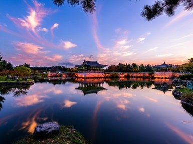 Ein malerischer Sonnenuntergang über dem Donggung Wolji Teich, mit reflektierenden Wolken und historischen Gebäuden im Hintergrund.