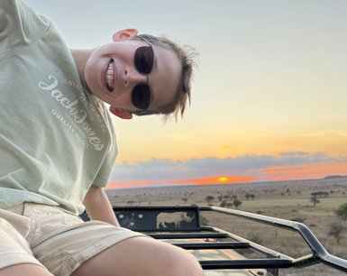 Ein Junge mit Sonnenbrille lächelt fröhlich aus einem Geländewagen, während die Sonne am Horizont untergeht.