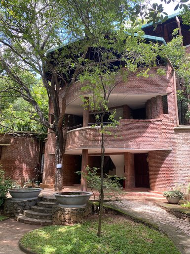 Ein modernes Gebäude mit rotem Ziegelstein, umgeben von üppigem Grün und großen Bäumen, strahlt eine einladende Atmosphäre aus.