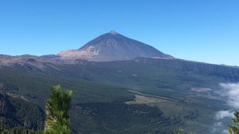 Der majestätische Teide erhebt sich über eine grüne Landschaft, umgeben von klarem, blauem Himmel und sanften Wolken.