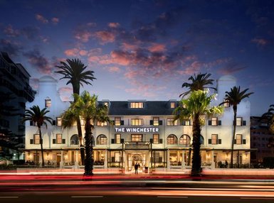 Das Winchester Hotel strahlt in der Dämmerung, umgeben von Palmen und einem farbenfrohen Himmel.
