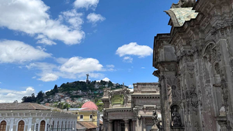 Ein lebhaftes Stadtbild mit historischen Gebäuden, Menschen auf der Straße und einem klaren blauen Himmel im Hintergrund.