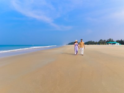 Ein Paar spaziert Hand in Hand am Strand, umgeben von sanften Wellen und einem klaren blauen Himmel.