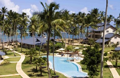 Ein tropisches Resort mit einem glitzernden Pool, umgeben von Palmen und Blick auf das Meer, ideal für Entspannung.
