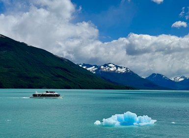 Ein modernes Boot fährt über das türkisfarbene Wasser, umgeben von majestätischen Bergen und schneebedeckten Gipfeln.