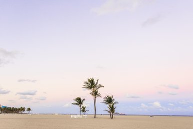 Ein ruhiger Strand mit sanften Wellen, umgeben von Palmen und einem sanften, pastellfarbenen Himmel bei Sonnenuntergang.
