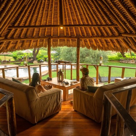 Eine gemütliche Lodge mit Strohdach, in der zwei Personen entspannt am Tisch sitzen und die Aussicht genießen.