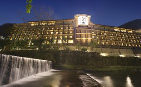 Ein elegantes Onsen-Hotel in Hakone, beleuchtet bei Nacht, mit einem sanften Wasserfall im Vordergrund.