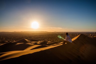 Frau sitzt auf einer goldenen Düne und blickt in die Weite der Sahara bei Sonnenuntergang – Marokko mit Kindern