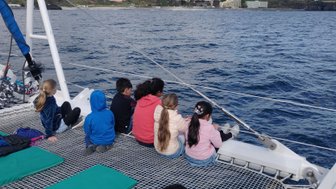 Eine Gruppe von Kindern sitzt auf einem Katamaran und blickt auf das ruhige Wasser, während sie die Aussicht genießen.