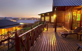 Eine Holzterrasse mit Blick auf ein Hotel, beleuchtet von warmem Licht, während die Dämmerung den Himmel färbt.