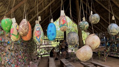 Bunte, handgefertigte Schalen hängen in einem traditionellen Dorf, umgeben von kunstvollen, bemalten Objekten an den Wänden.