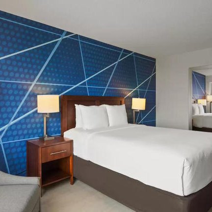 Ein modernes Hotelzimmer mit einem großen Bett, stilvollen Lampen und einer auffälligen blauen Wandgestaltung.