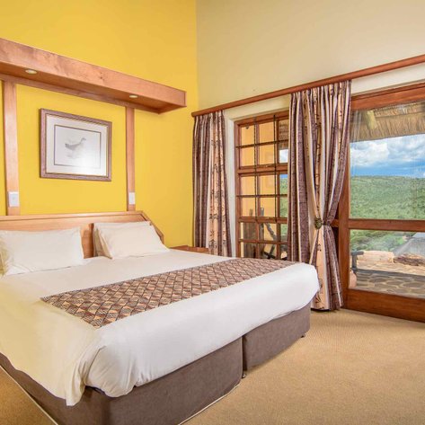 Ein helles Zimmer mit einem großen Bett, umgeben von gelben Wänden und einem Fenster, das auf eine grüne Landschaft blickt.