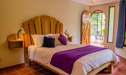 Ein einladendes Zimmer mit einem großen Bett, das mit lila und weißen Kissen dekoriert ist, und einem Holzpaneelkopfteil.