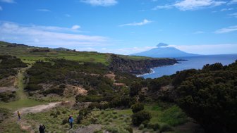 Eine malerische Küstenlandschaft mit einem Vulkan im Hintergrund, umgeben von üppigem Grün und klarem Himmel.