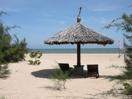 Ein schattiger Sonnenschirm aus Stroh steht am Strand, umgeben von sanften Wellen und feinem Sand.