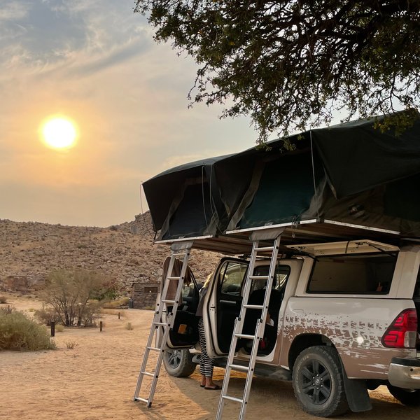 Ein Jeep steht mit aufgebautem Dachzelt auf einer Sandfläche