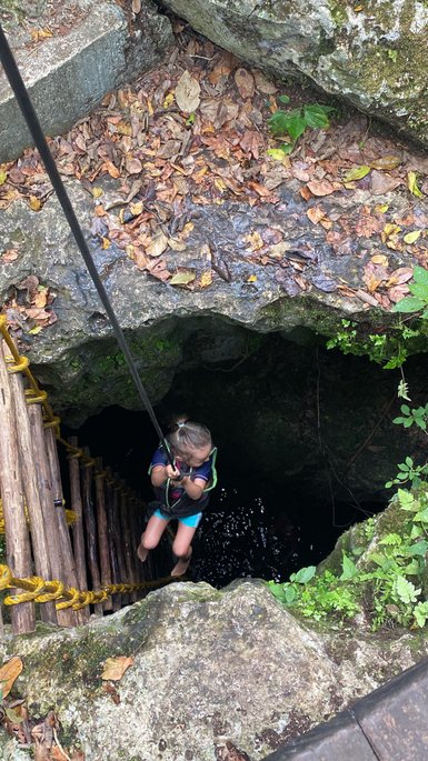 Ein Kind steigt vorsichtig über eine steile Holzleiter in eine dunkle Höhle im Punta Laguna Park hinab – Mexiko Familienreise