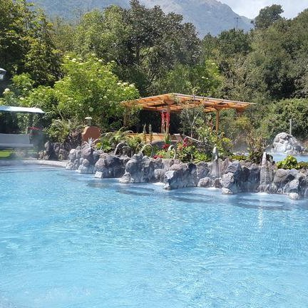 Ein entspannender Spa-Bereich mit einem blauen Thermalpool, umgeben von üppigem Grün und sanften Dampfwolken.