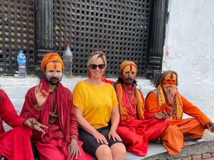 Eine Frau in gelbem Shirt sitzt mit vier farbenfroh gekleideten Männern, die traditionelle Gesichtsbemalung tragen, auf einer Treppe.