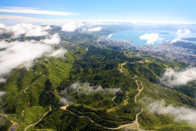 Eine atemberaubende Luftaufnahme von Wellington, die grüne Hügel und die Küstenlinie der Stadt zeigt, umgeben von Wolken.