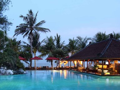 Ein ruhiger Poolbereich in Bali, umgeben von Palmen und einem traditionellen balinesischen Pavillon im Abendlicht.
